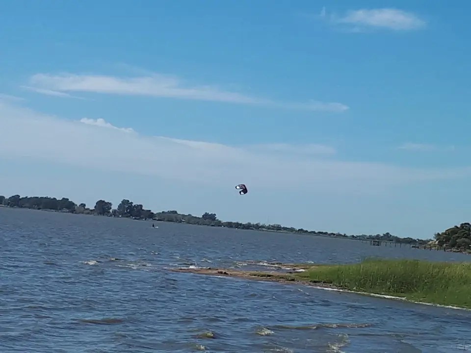 Una vela de kitesurf sobre la laguna, con la orilla de pasto.
