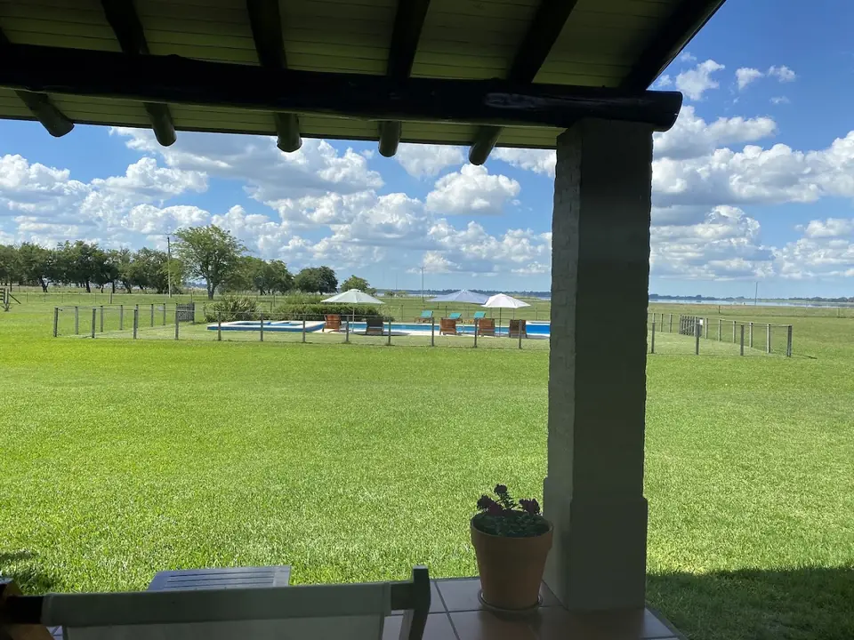 La mañana desde la galería de una casa: el parque, la pileta y la laguna en el horizonte.