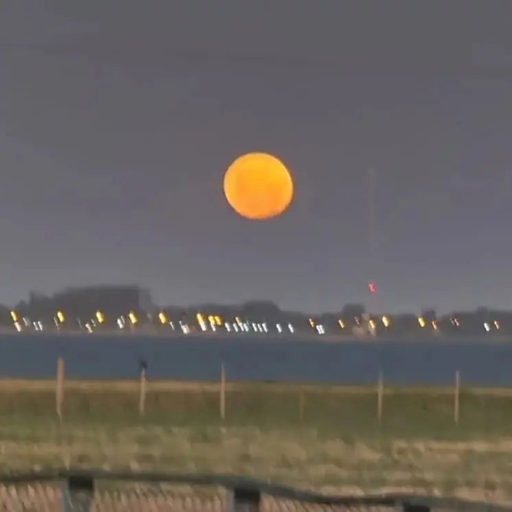 La luna llena sobre la laguna, con las luces de Chascomús en la otra orilla.