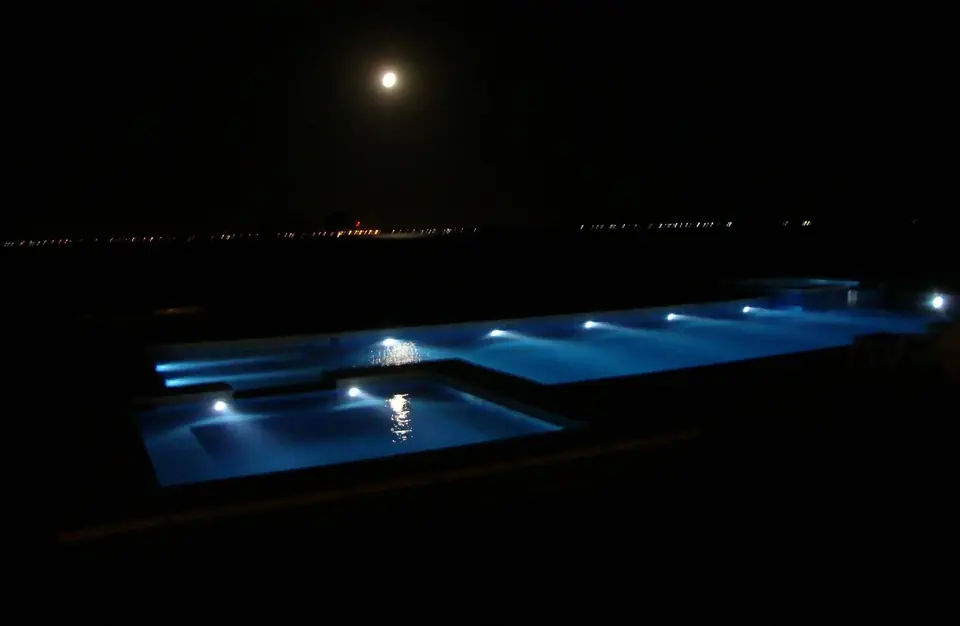 La pileta iluminada de noche, con la luna y las luces de Chascomús en el horizonte.
