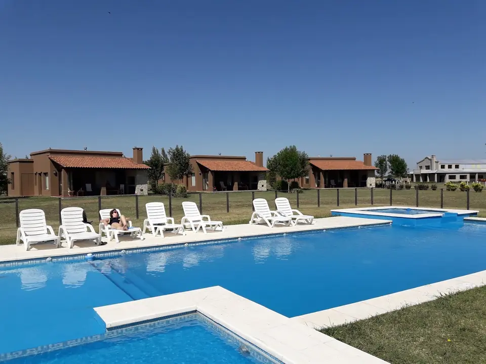 La pileta grande con las reposeras y las tres casas al fondo.