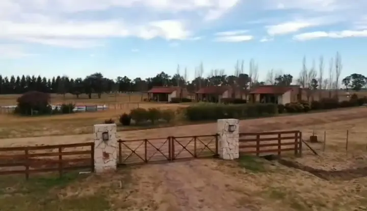 La tranquera de madera entre pilares de piedra, con las casas al fondo.